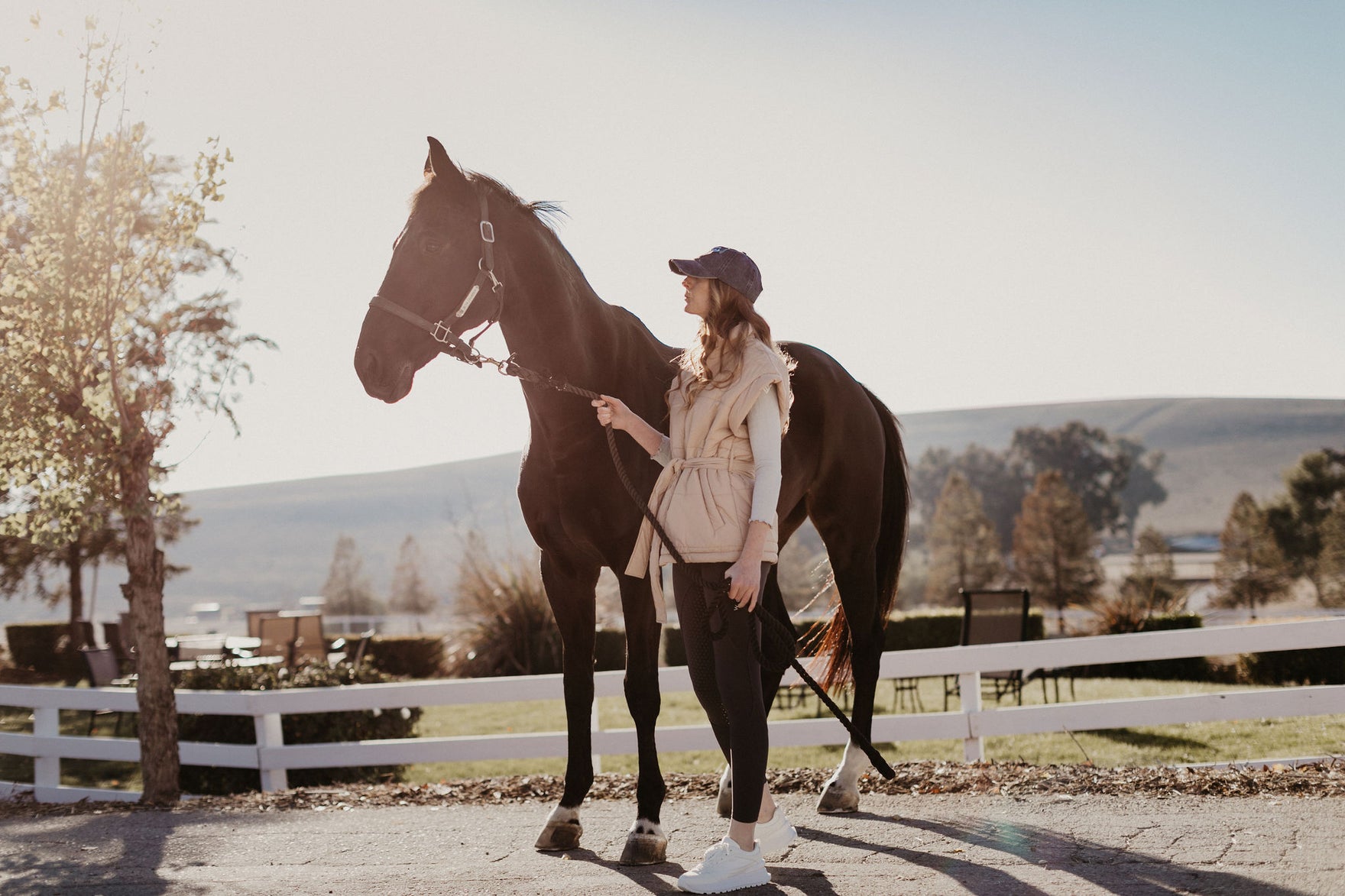 Impeccably designed eco-friendly equestrian apparel for conscious horse riders. Picture a scene in a warm, sun-lit equestrian farm. A female, Hispanic rider in her sustainable leather-free boots, and 